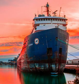 A large ship moored at a dock beneath a vivid coral-red sunset sky.