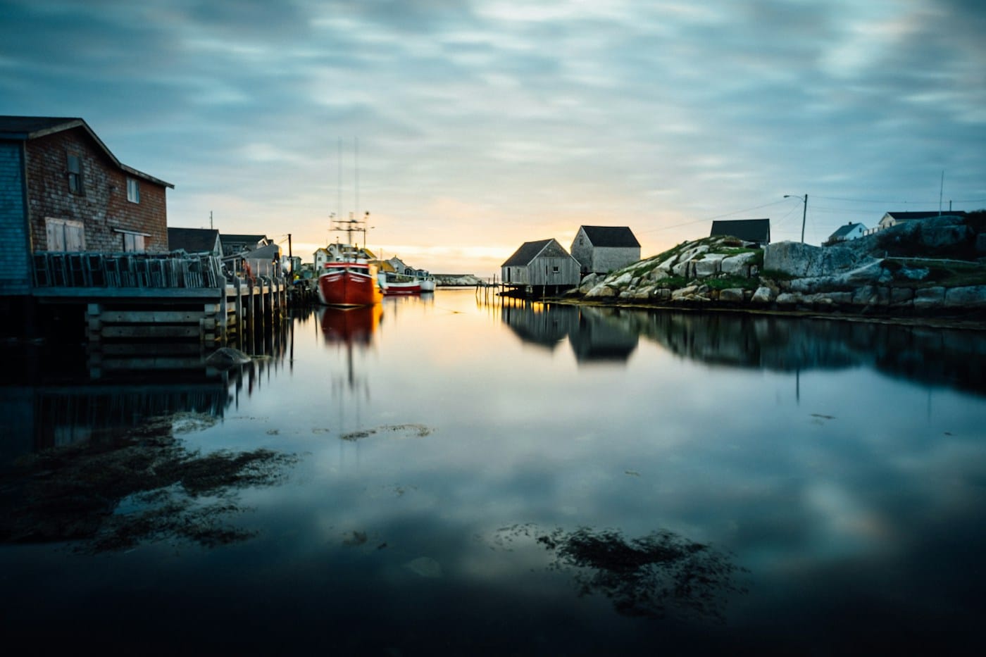 A fishing harbour at first light, weathered sheds reflected in still water.
